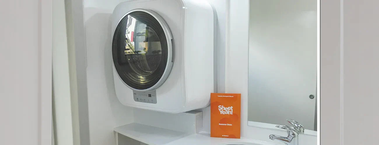 Travel washing machine in a caravan with a packet of Sheet Yeah! laundry washing sheets beside it