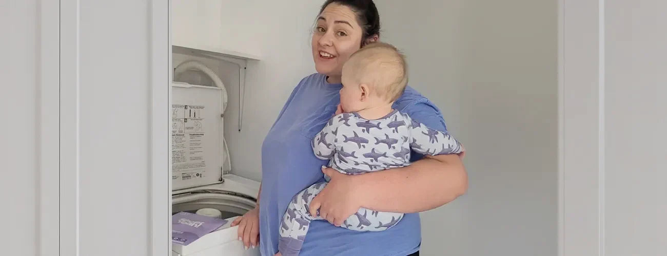 Mum holding her baby while doing the laundry 