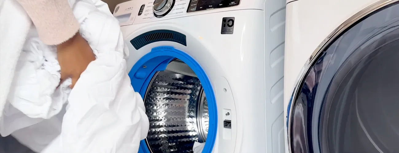 Women putting a load of white sheets into a front loader washing machine