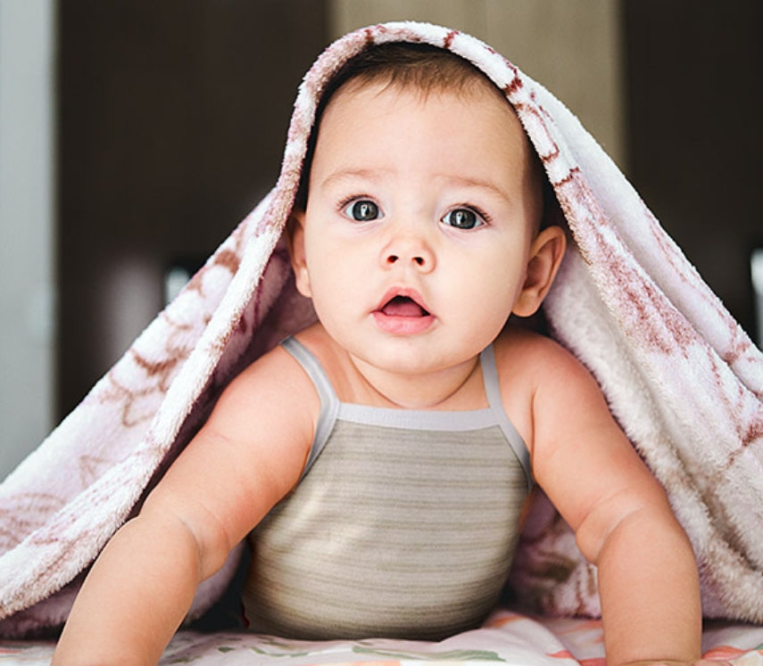 Baby sticking its head out from under a blanket and looking directly at the camera 